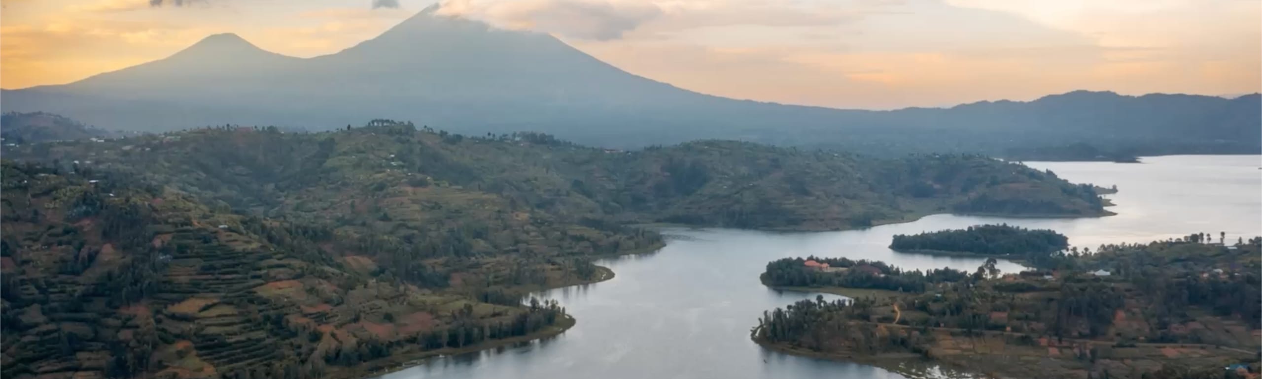 Lake Kivu at dawn, with volcanic peaks rising behind terraced Rwandan hillsides.